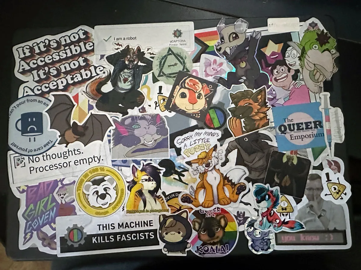 A top-down photograph of a laptop that has been sticker bombed with dozens, if not hundreds, of stickers.