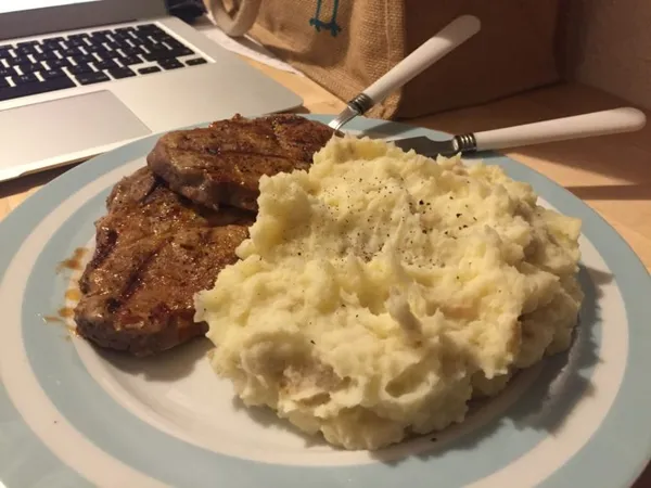 Photograph of a plate with steak and mashed potatoes, sprinkled with a little pepper.